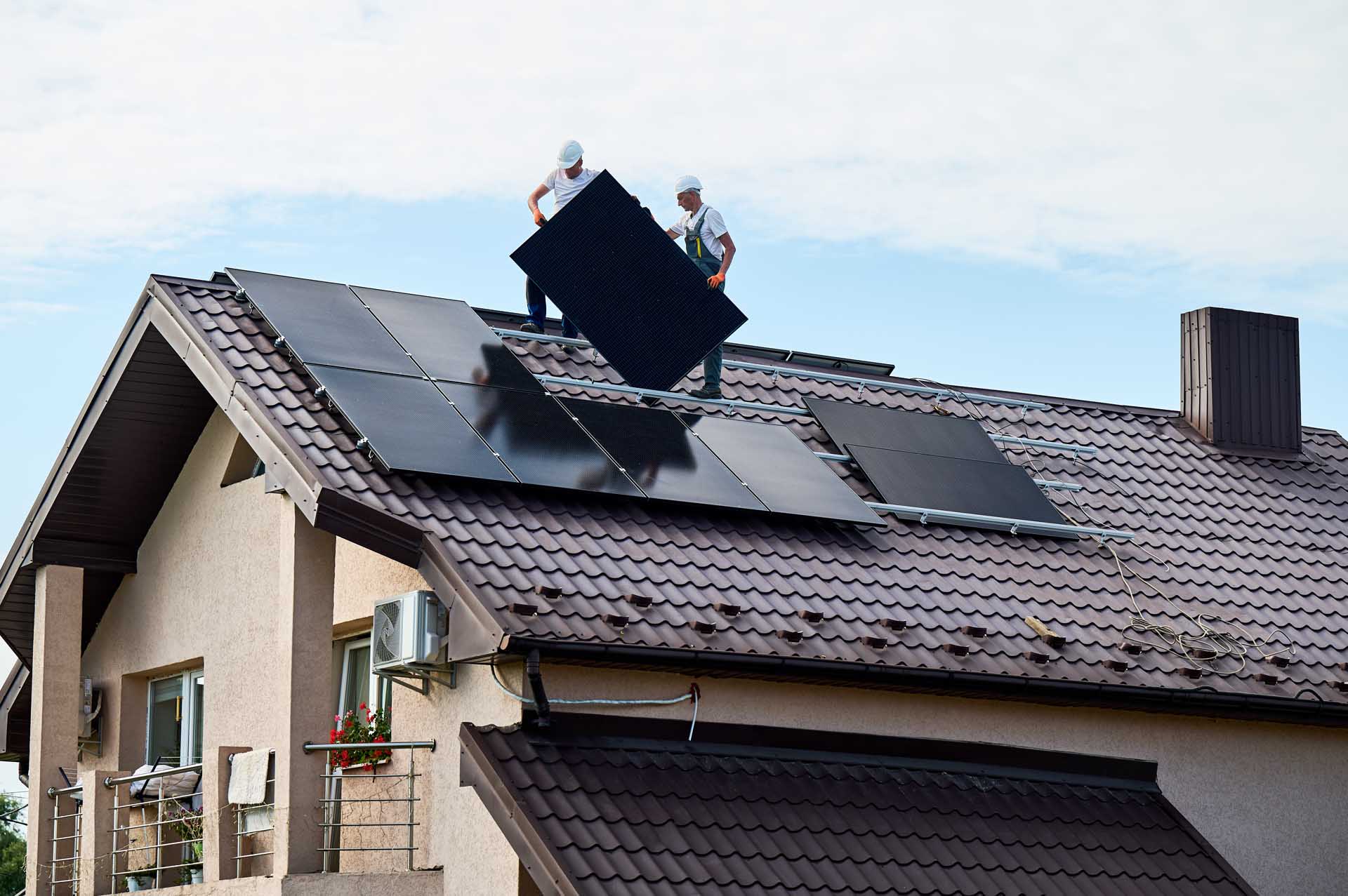 Installers positioning solar panels on a residential rooftop.