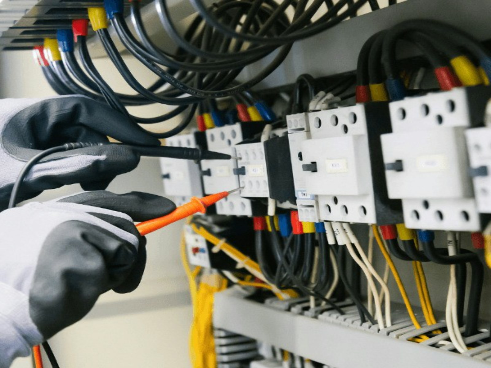 Electrician testing wiring inside an electrical service panel with a multimeter.